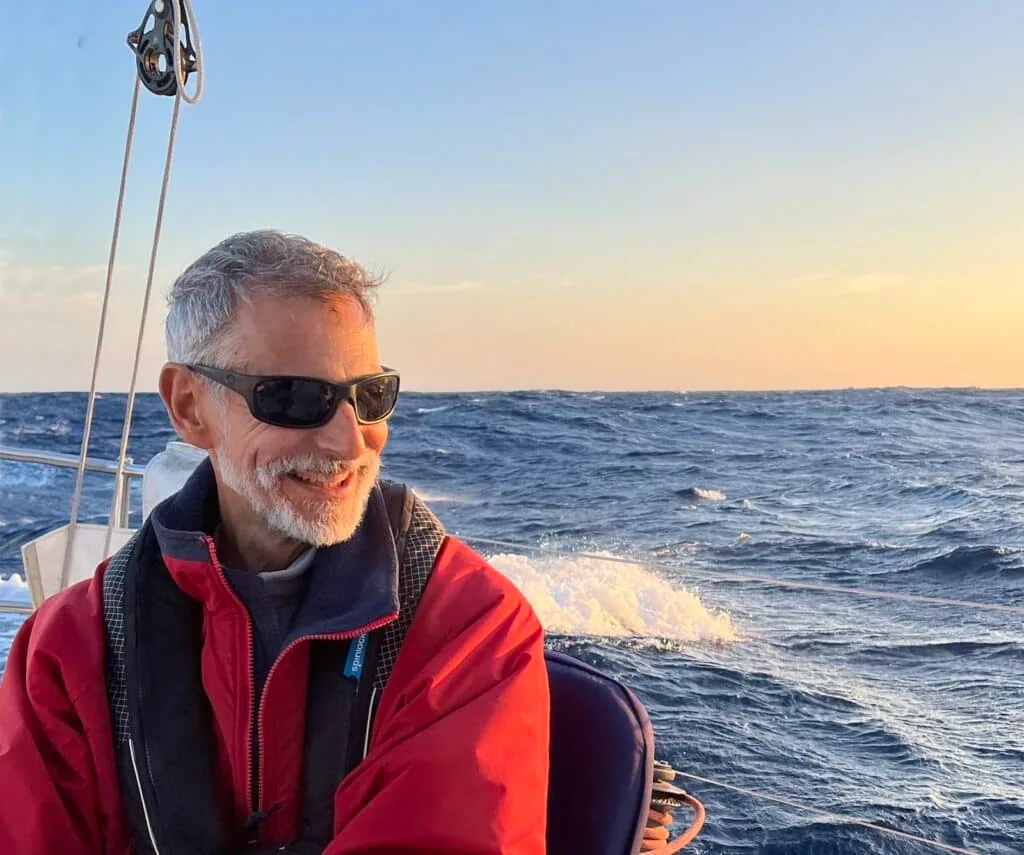 Sailor smiling on deck under a warm sunset sky offshore