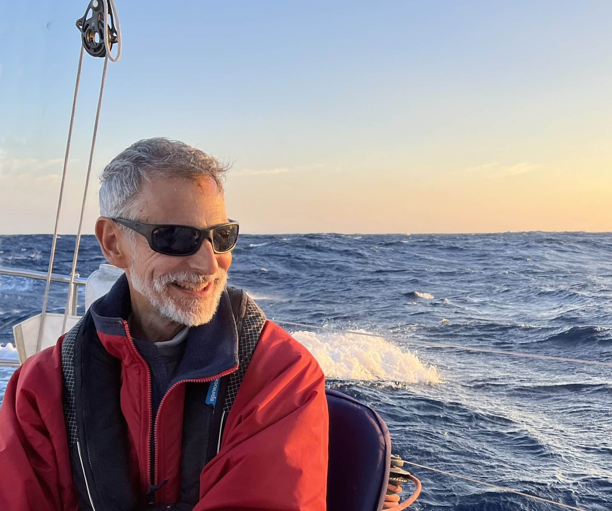 Adam Loory smiling on deck under a warm sunset sky offshore