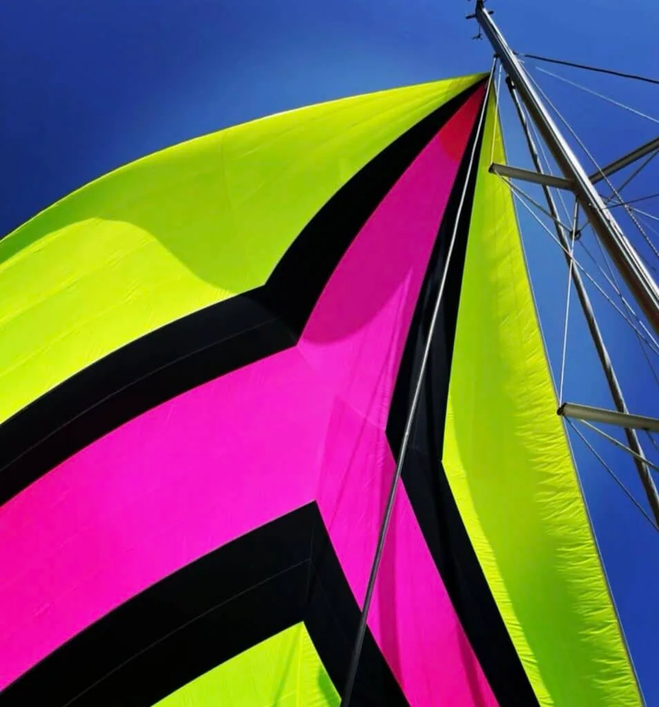 Lime-green and magenta asymmetric spinnaker filled against a blue sky