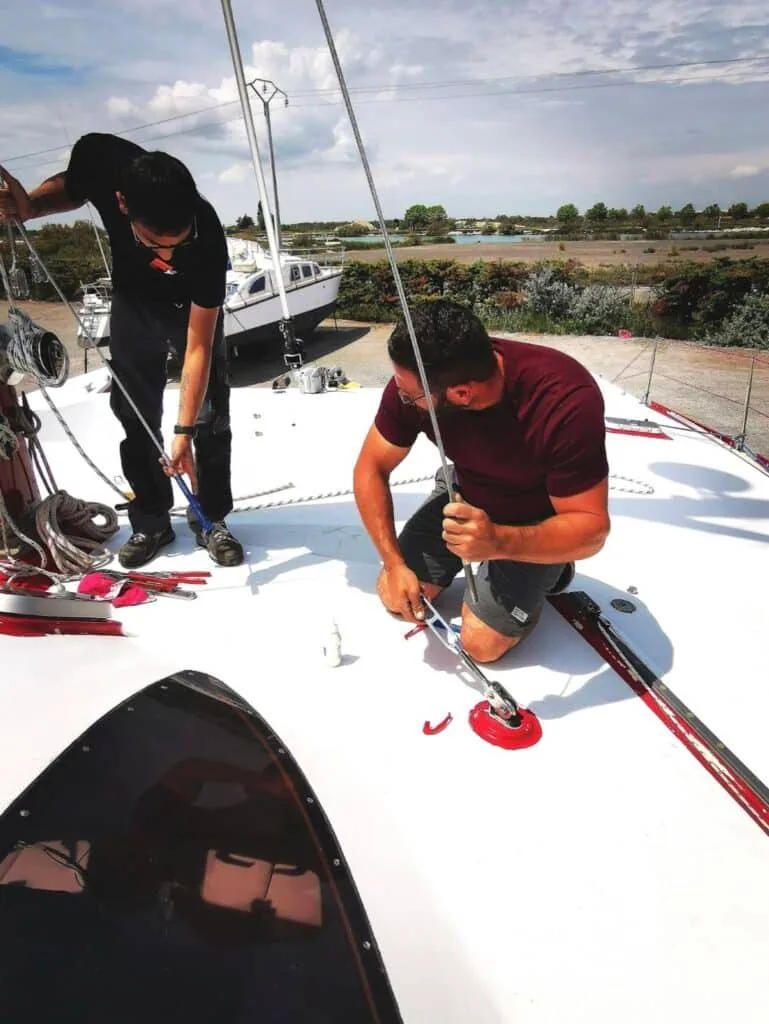 Two riggers installing deck hardware on a sailboat in a French boatyard