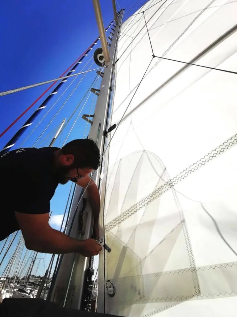 Rigger fitting a mainsail's luff slides at the mast in a marina