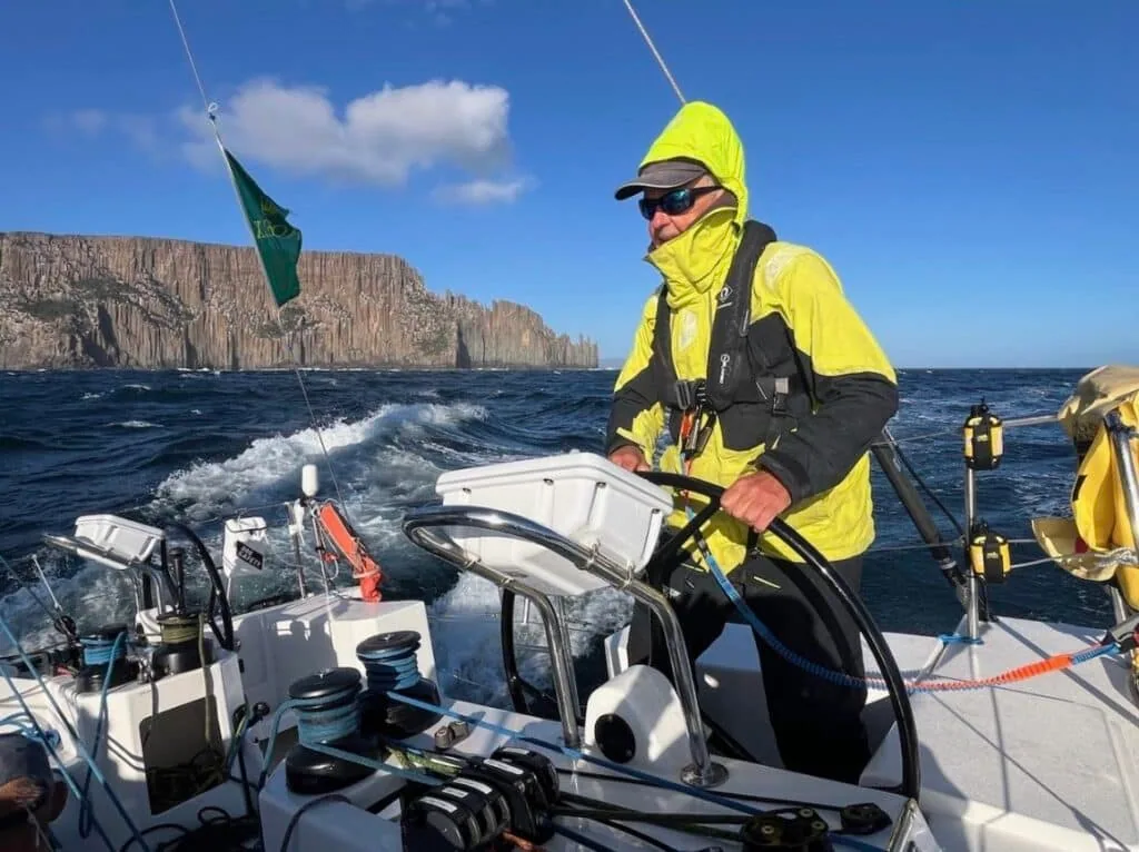 Helmsman at the wheel passing dramatic sea cliffs during the Sydney Hobart