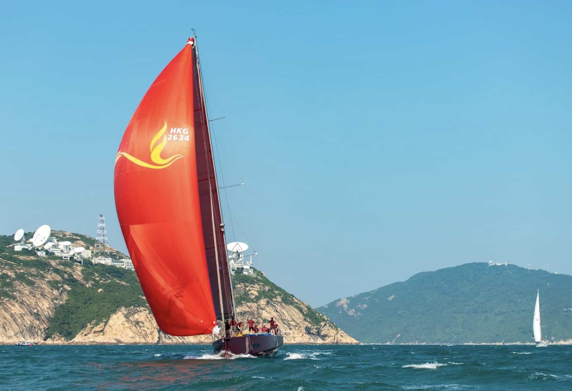 FENICE running under a red spinnaker past a rocky Hong Kong headland
