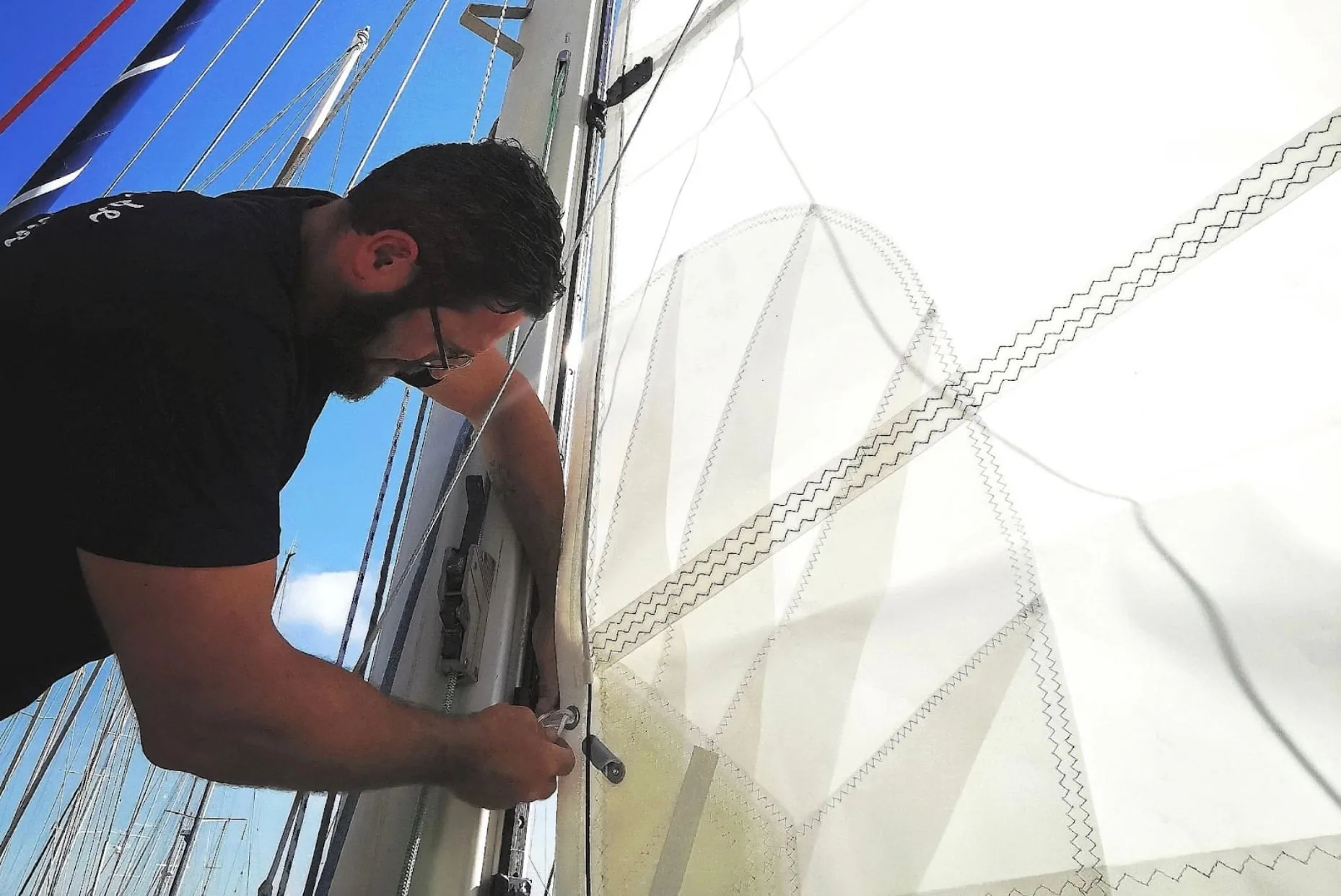 Rigger fitting sail slides to a mast track in bright sunlight