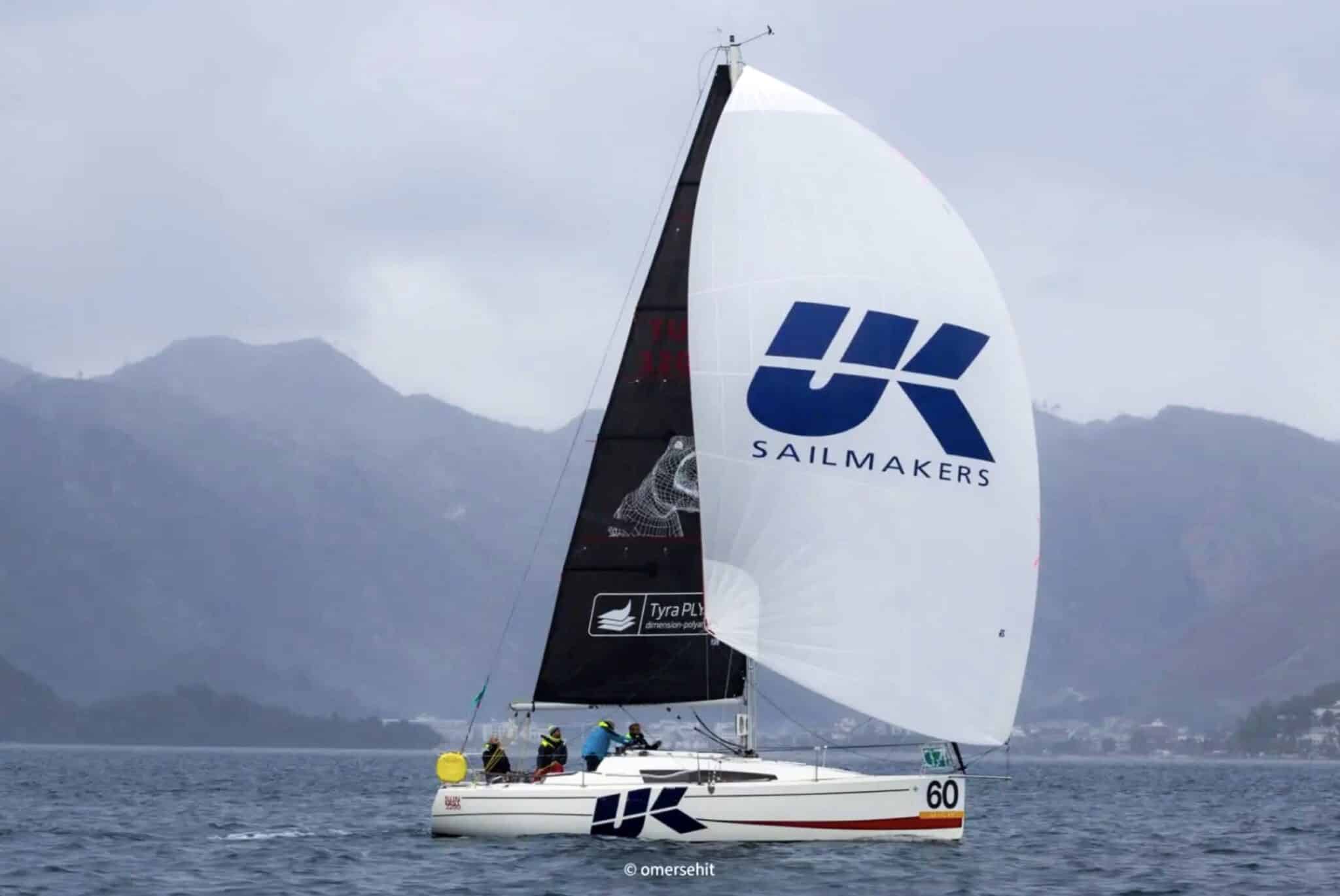 Yacht number 60 flying a large UK Sailmakers spinnaker in front of a mountainous coastline