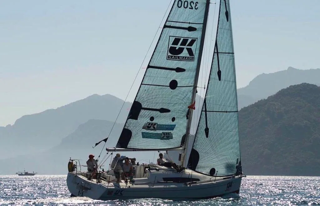 Sun Fast 3200 sailing upwind under UK Sailmakers Titanium BLUE sails along a mountainous coast
