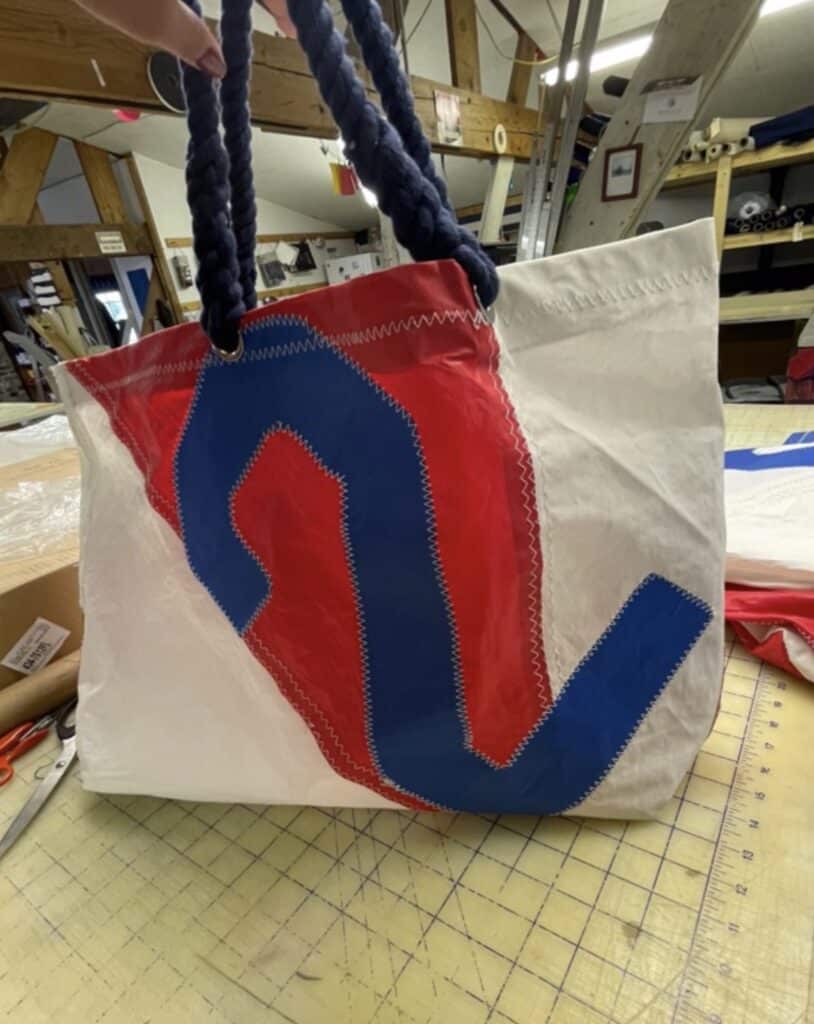 Tote bag sewn from recycled sailcloth with a red-and-blue graphic, held up in a sail loft