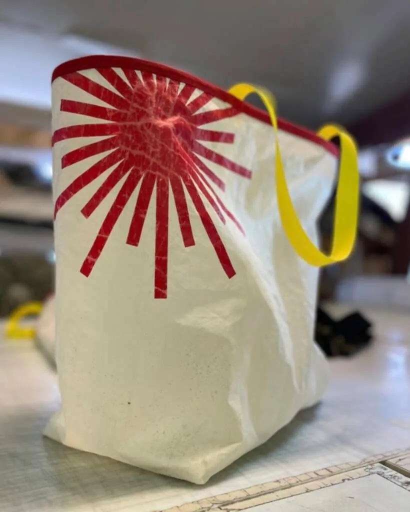 Cream tote bag made from recycled sailcloth with a red sunburst design and yellow handles
