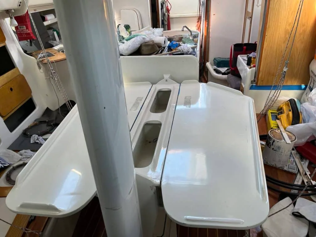 Drop-leaf saloon table open inside a boat's interior amid ocean-cruising refit work