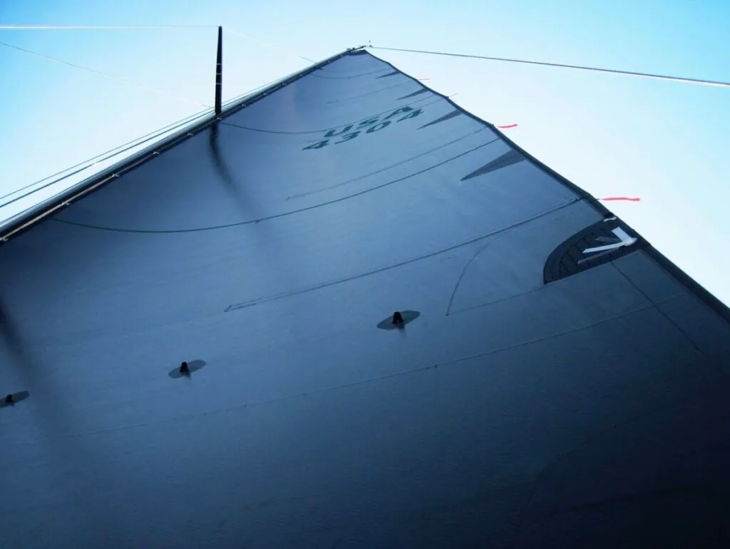 Black mainsail viewed from below, its numbers barely visible against the dark cloth