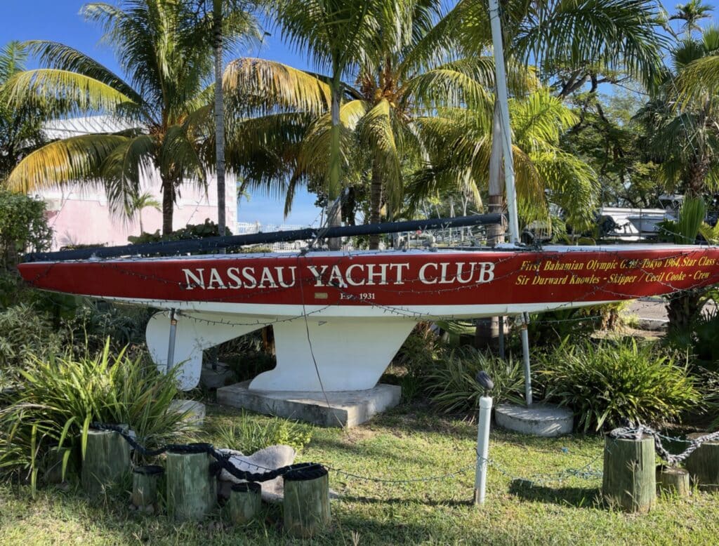 Weathered red-hulled Nassau Yacht Club monument boat displayed among palm trees