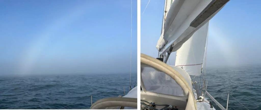 Pale fog bow arching over calm water, seen from a sailboat's cockpit