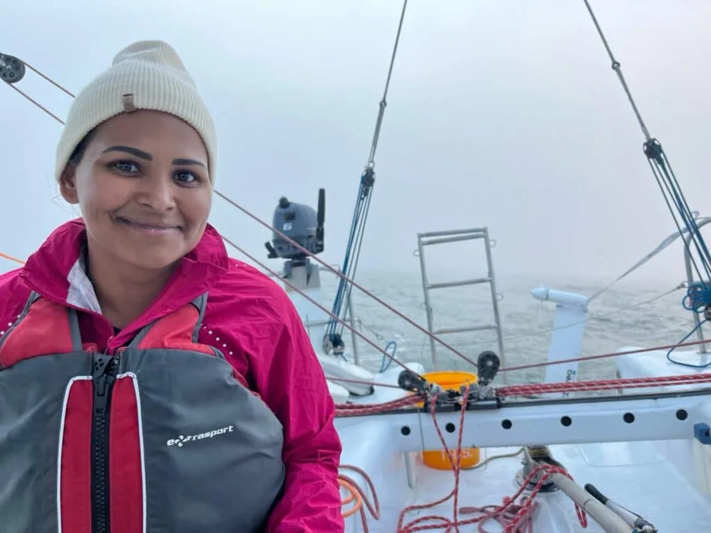 Sailor in a pink jacket and beanie on deck during a foggy offshore passage
