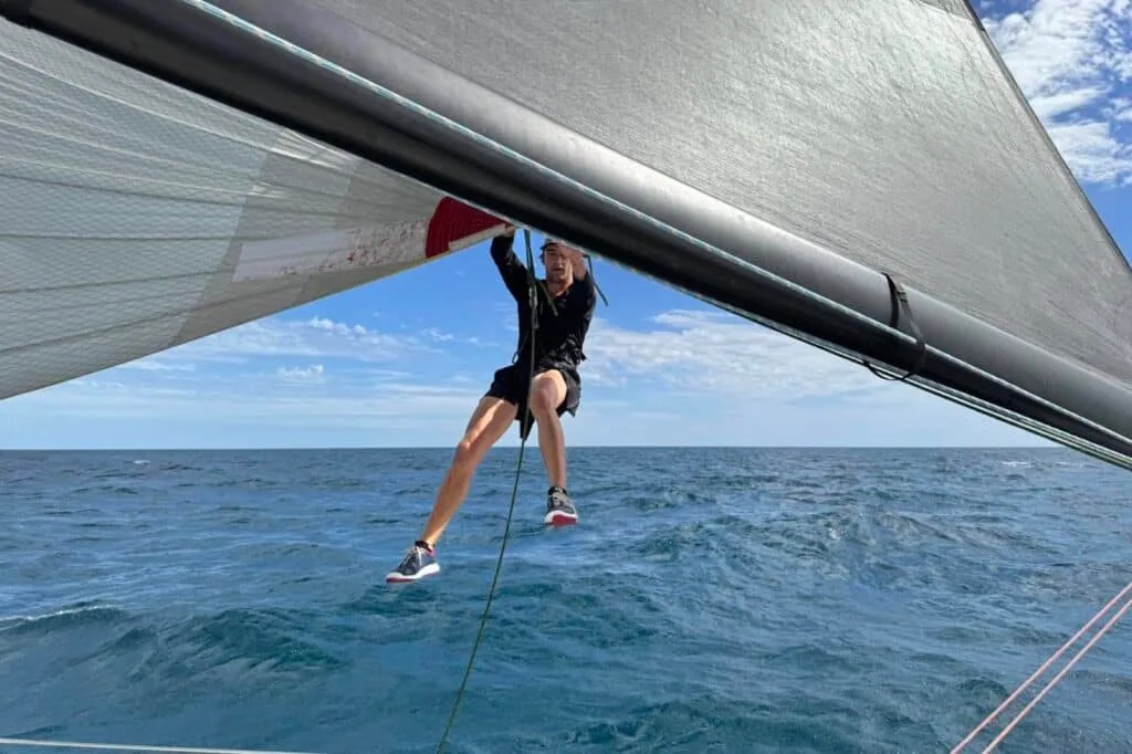 Crew member hangs off the boom on a line, skimming the water underway