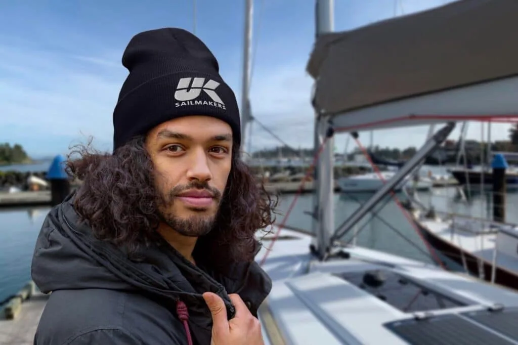 Man wearing a black UK Sailmakers beanie on a sailboat's deck