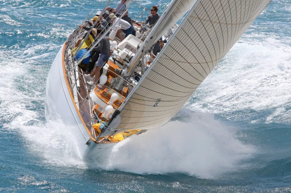 Classic racing yacht buries its bow in a wave, crew braced on the rail