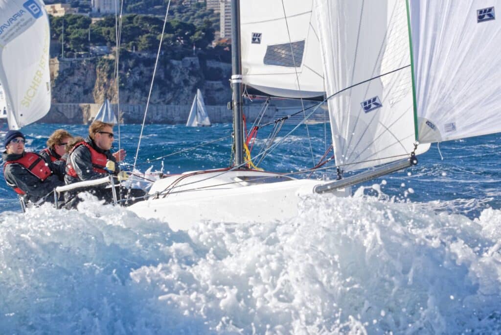 Keelboat crew hikes out hard under a UK Sailmakers jib off a coastal town