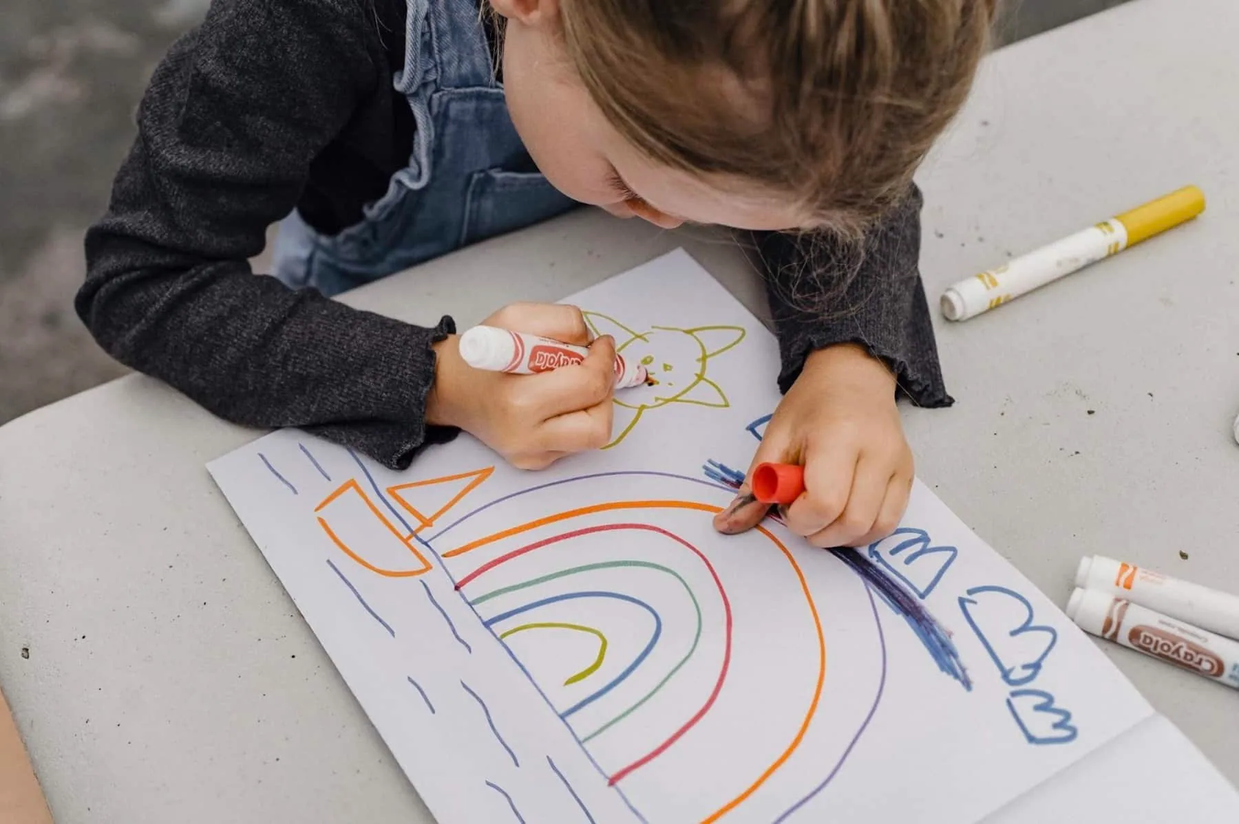Child draws a rainbow and sailboat with markers for the T-shirt contest