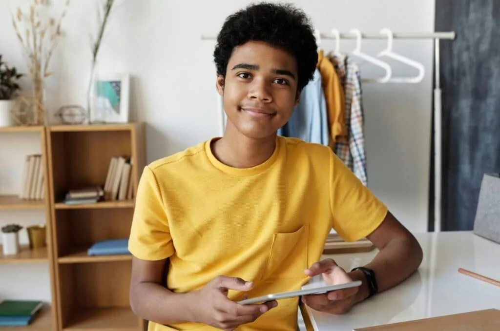 Teen in a yellow T-shirt holds a tablet at a desk