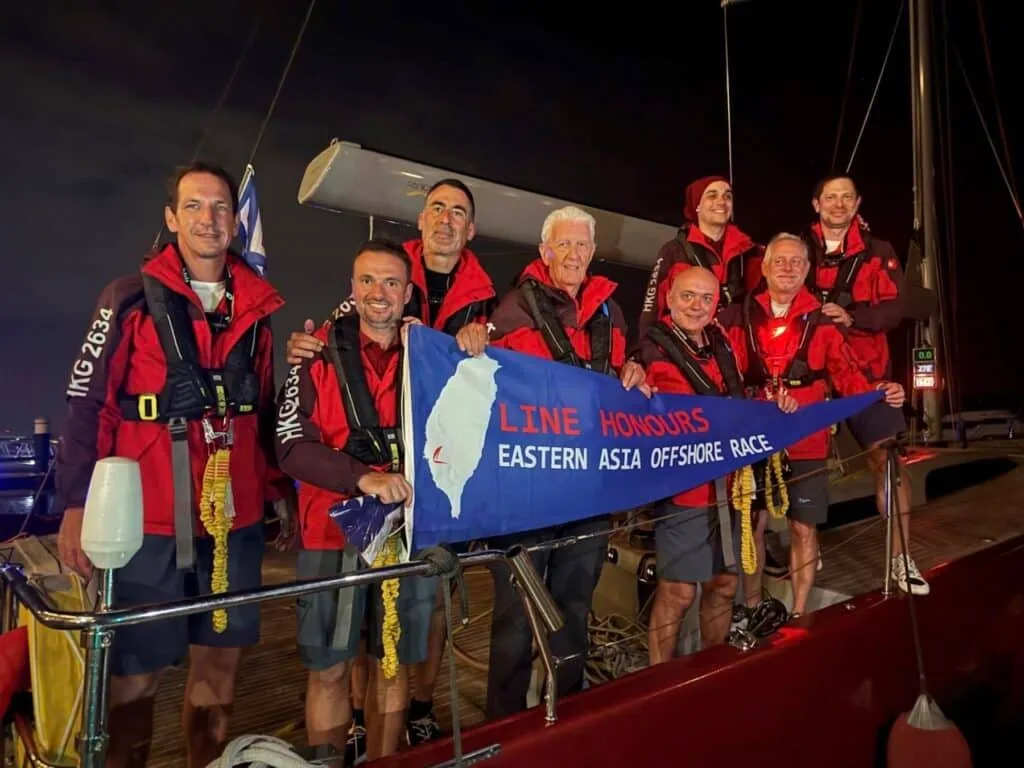 Crew holds a Line Honours burgee for the Eastern Asia Offshore Race at night