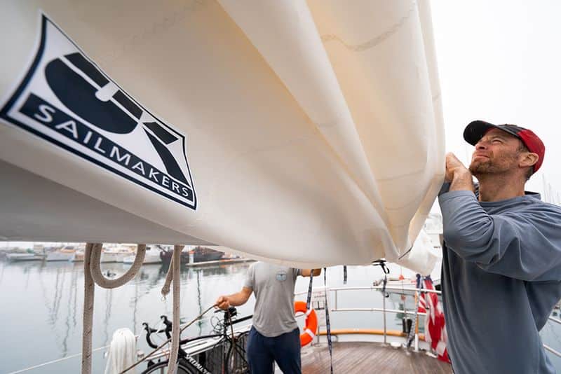 Two sailors hoisting a mainsail stitched with the UK Sailmakers burgee logo at the dock
