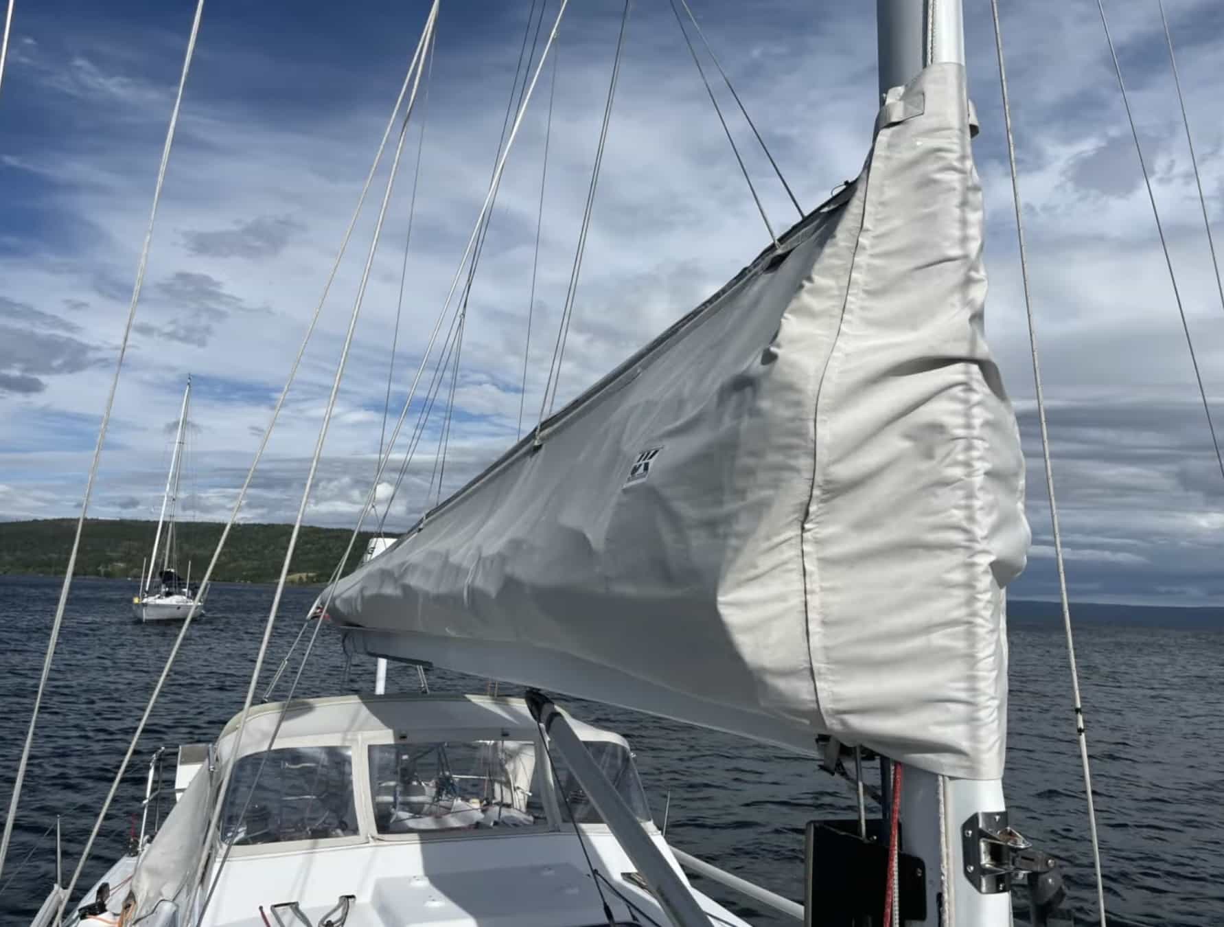 Furled mainsail resting in a lazy cradle stack pack, viewed from the cockpit at anchor
