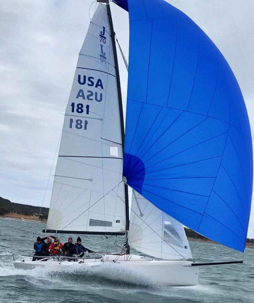 J/70 USA 181 planing downwind under a blue spinnaker with four crew hiking out