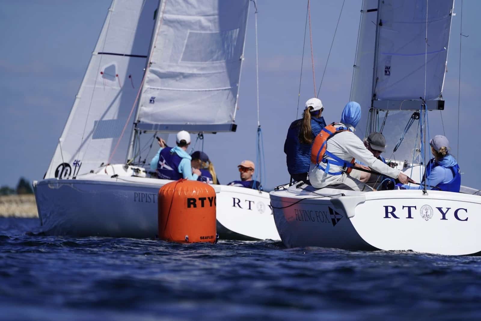 Team-racing boats rounding an orange mark, crew in blue vests, during the Cumberland Cup