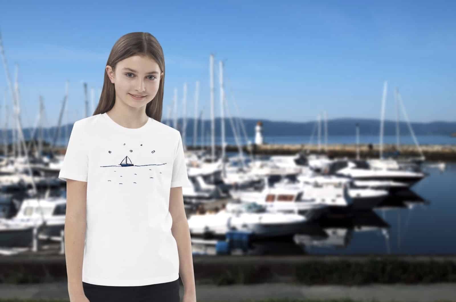 Girl wearing a white T-shirt printed with a small sailboat design, marina in the background