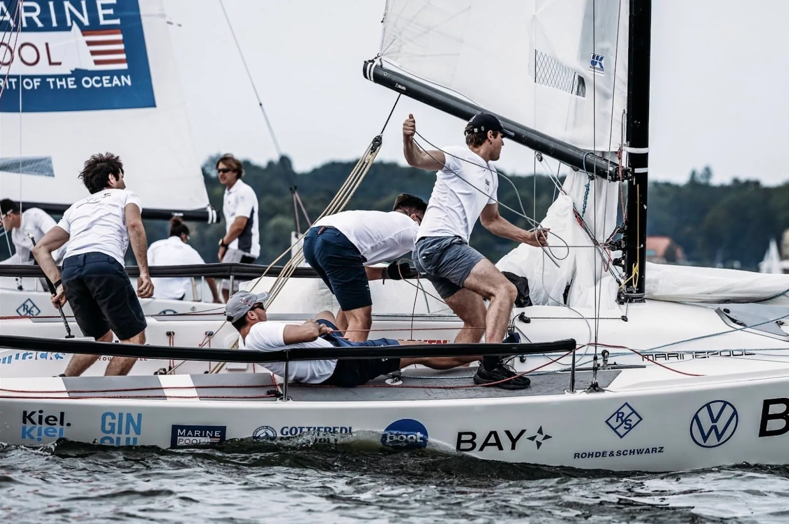 J/70 crew hiking hard under sponsor banners at the Deutsche Segel-Bundesliga in Kiel