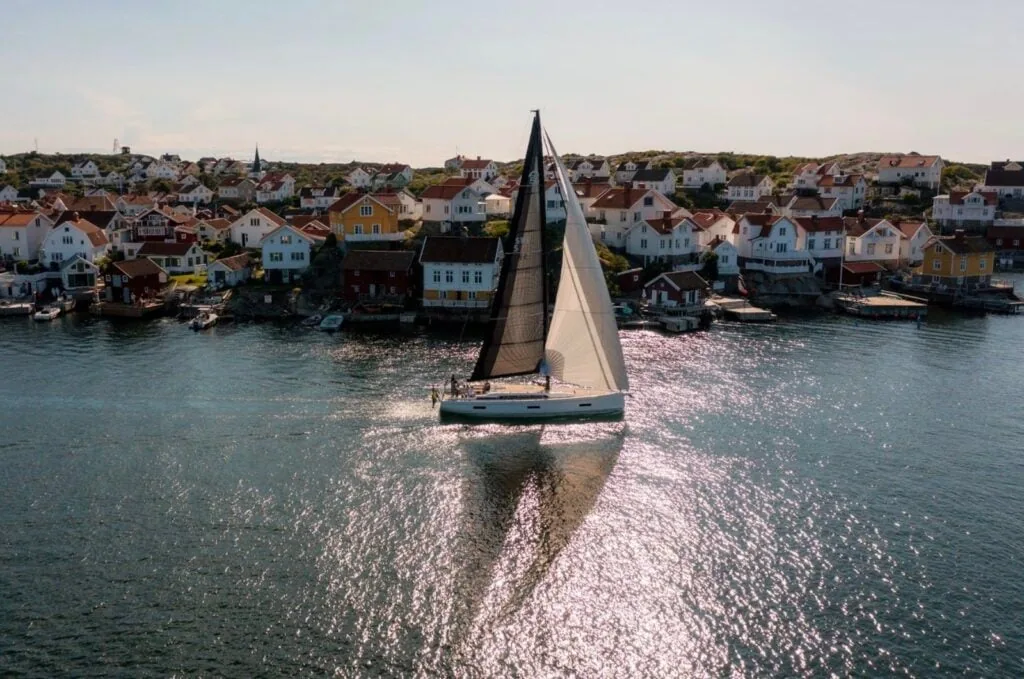 Backlit sailboat gliding past a colorful waterfront village at golden hour