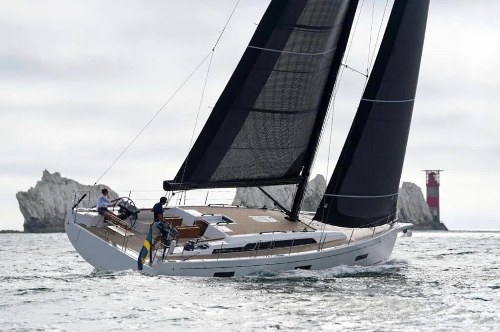 Performance cruiser sailing near a rocky coast and lighthouse under dark, high-tech sails