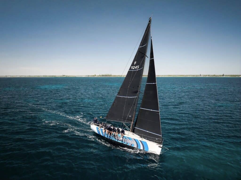 Yacht F 1245 heeled under dark sails with crew on the rail in turquoise water