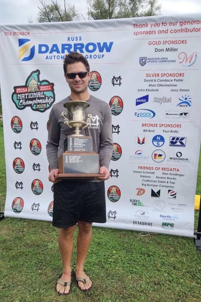 Sailor holding the 2025 MCSA National Championship trophy at the awards banner