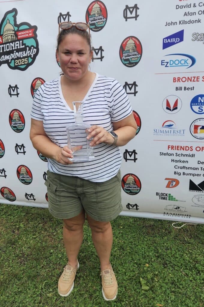 Sailor holding a glass trophy at the 2025 MCSA National Championship sponsor banner