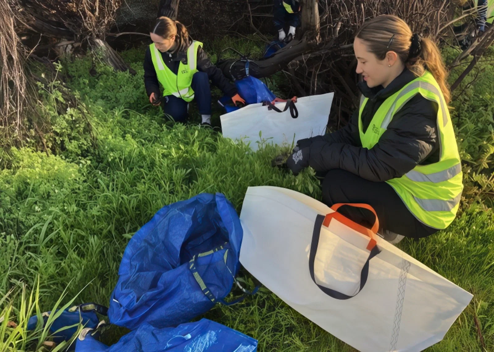Volunteers in hi-vis vests filling a recycled-sailcloth bag with garden cuttings