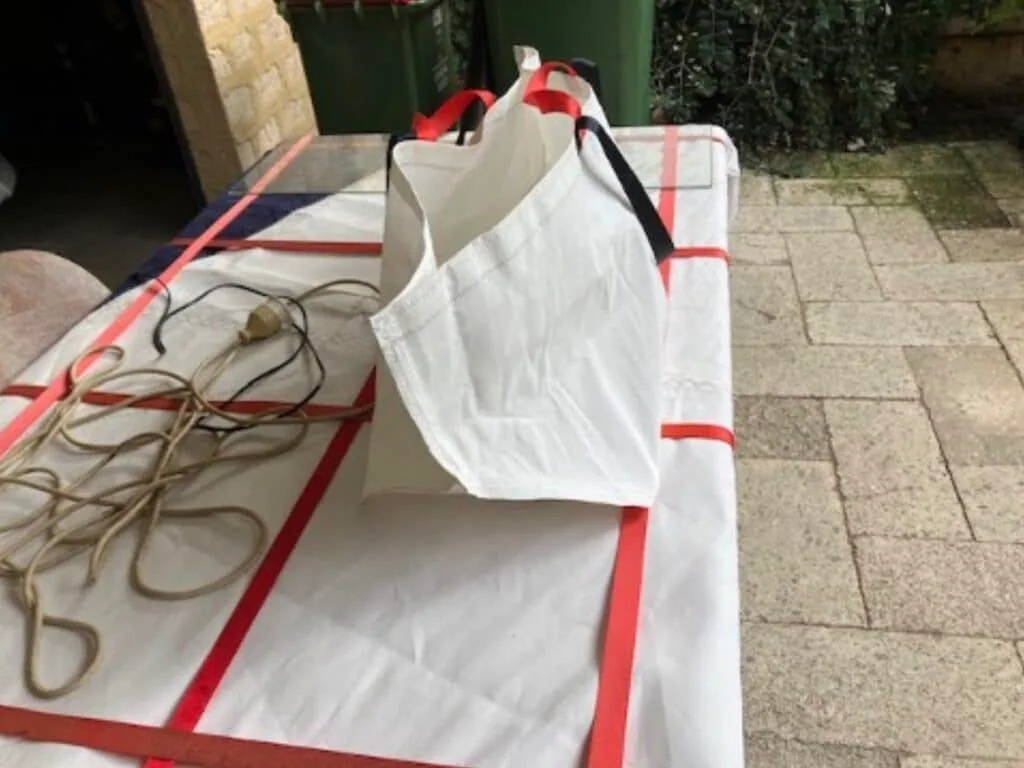 Finished white tote bag with red webbing handles, cut from recycled sailcloth on the loft table