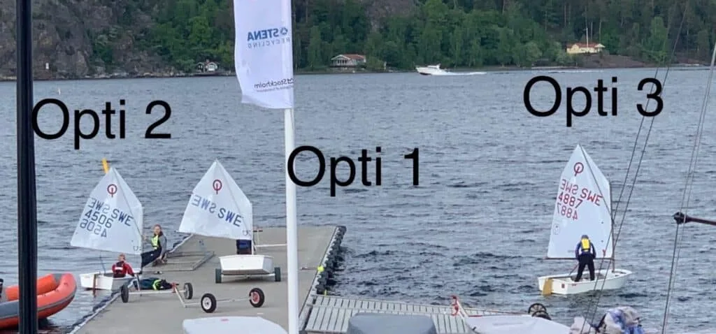 Three Optimist dinghies labeled Opti 1, 2, and 3 rigged at the dock before racing