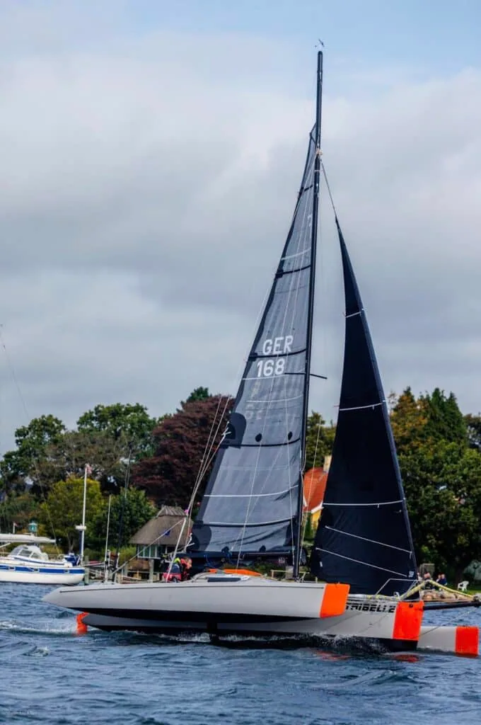 Narrow racer with orange outrigger floats and dark sails, sail number GER 168, in the Silverrudder fleet