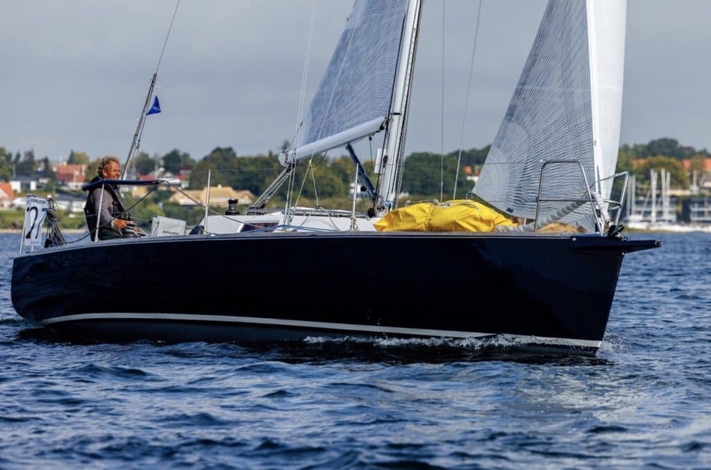 Dark blue-hulled sloop under mainsail and jib, solo helmsman visible, in the Silverrudder fleet