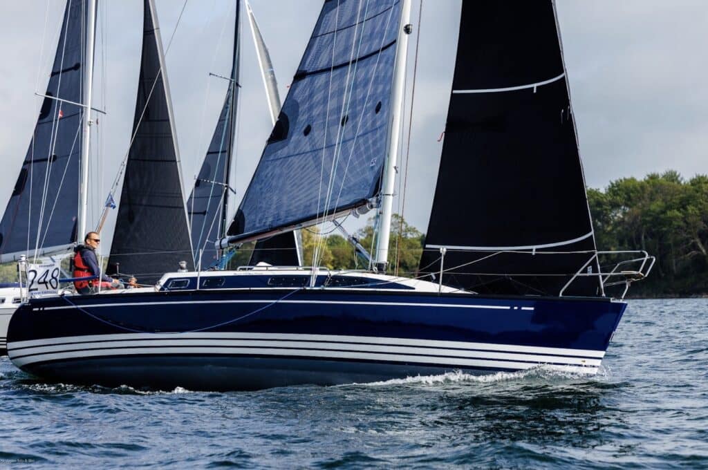 Navy-hulled racer numbered 248 close-hauled under dark sails, solo sailor at the helm