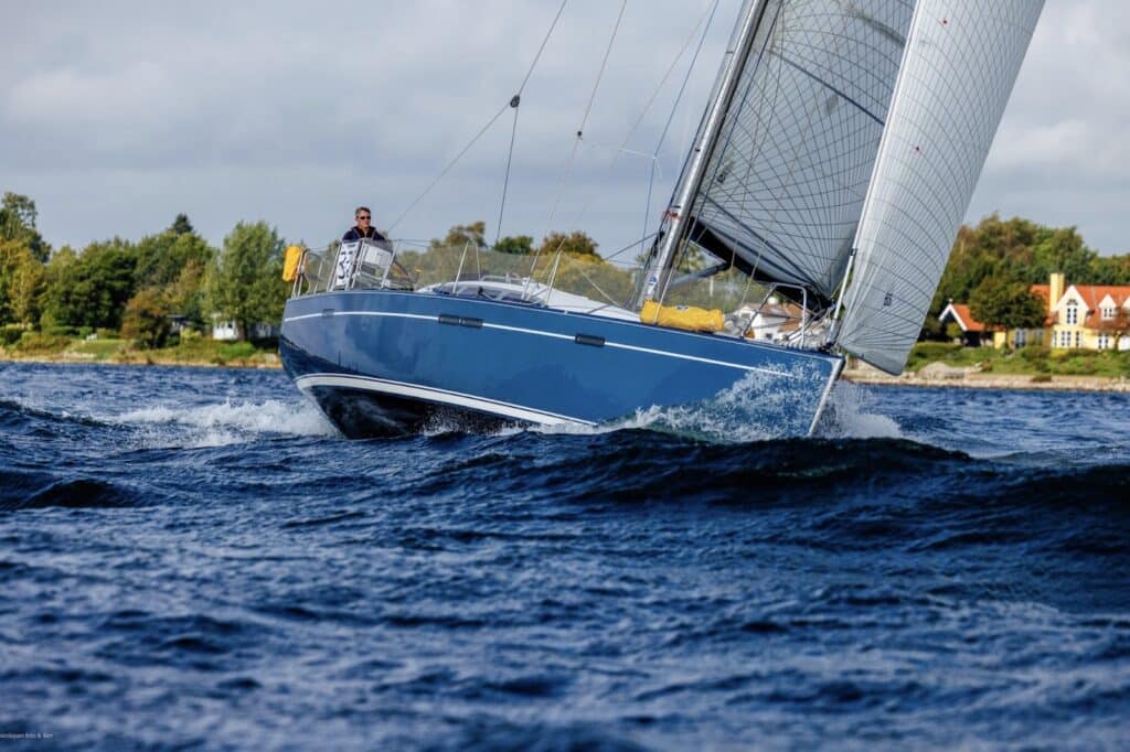 Blue-hulled sloop heeled over with spray flying, crew hiked out, in the Silverrudder fleet