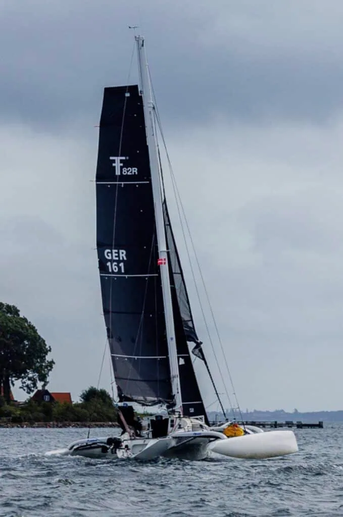 Trimaran T82R (GER 161) under a tall black mainsail nearing the shore in the Silverrudder Challenge