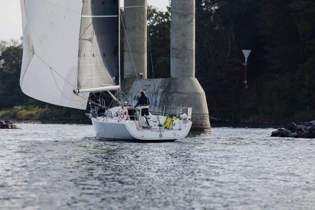 White sloop passing beneath a large road bridge during the Silverrudder Challenge