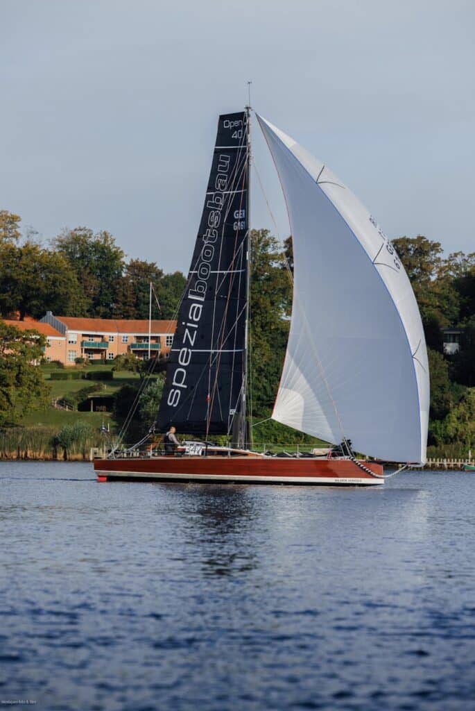 Red-hulled Open 40 Spezialbootsbau racer flying a white spinnaker at dusk in the Silverrudder Challenge