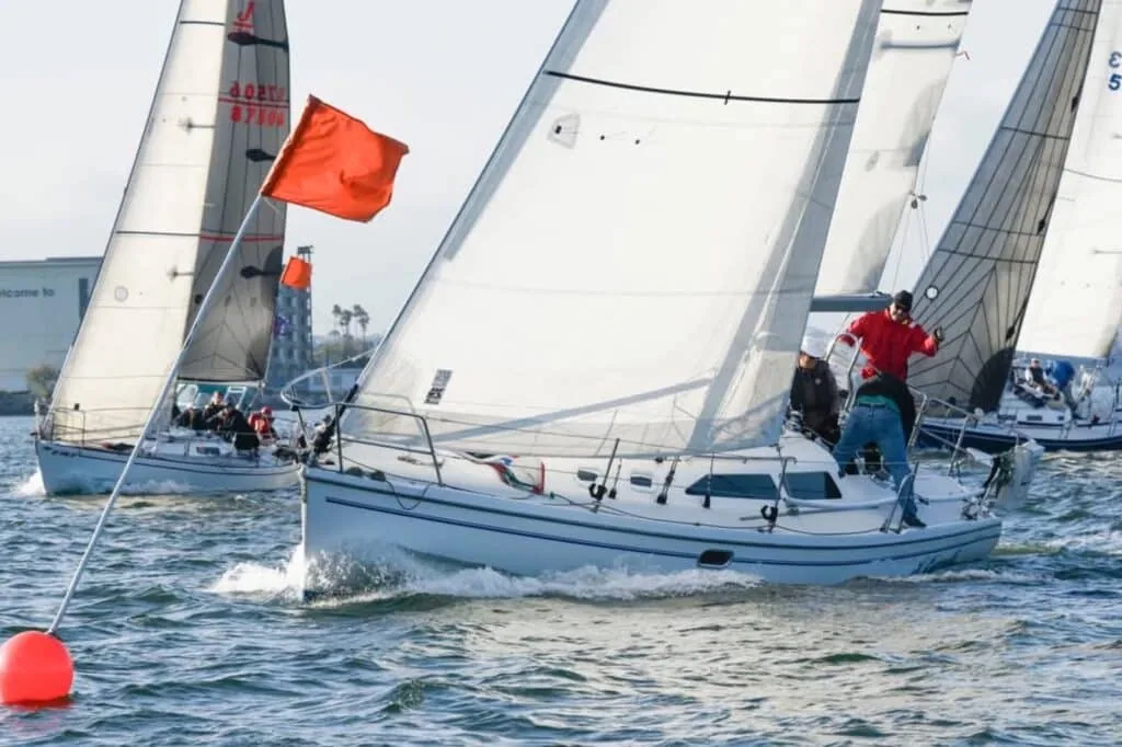 Sailboat rounding a red-flagged mark closely trailed by another boat