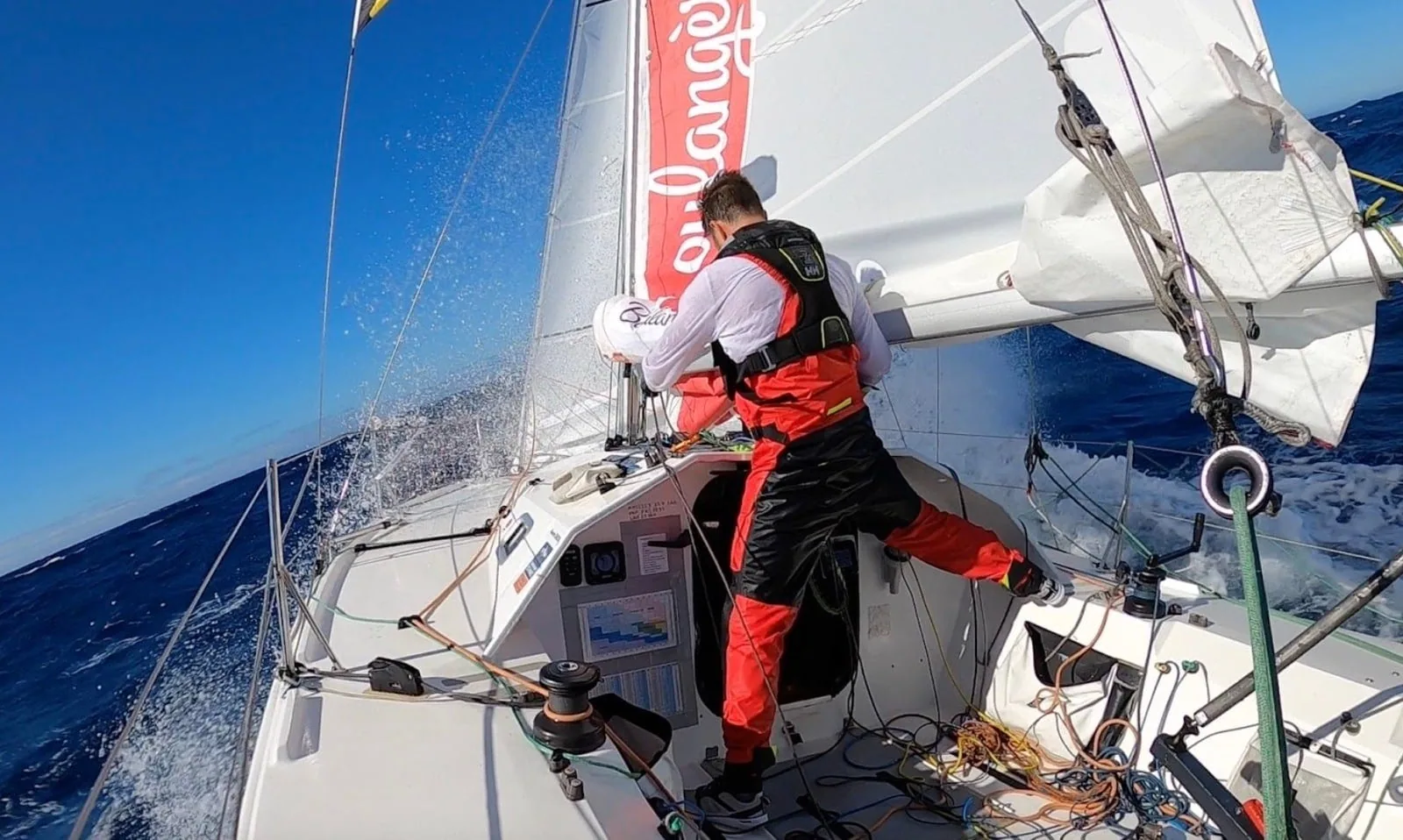 Sailor working the foredeck in red foul-weather gear on an offshore solo racer
