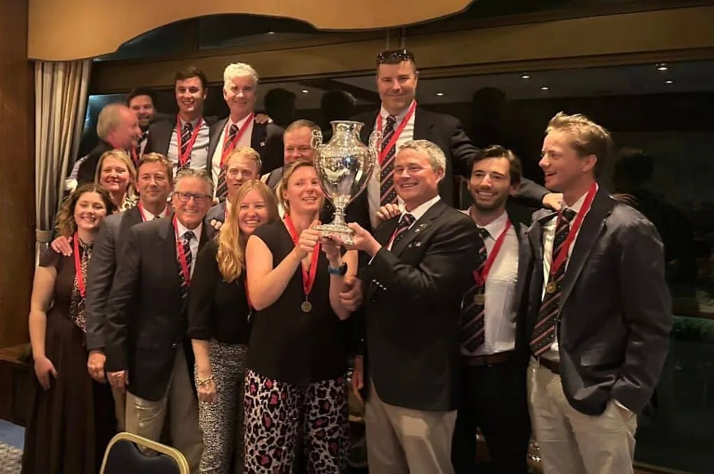 Team posing with a silver trophy at a formal awards dinner, medals around their necks