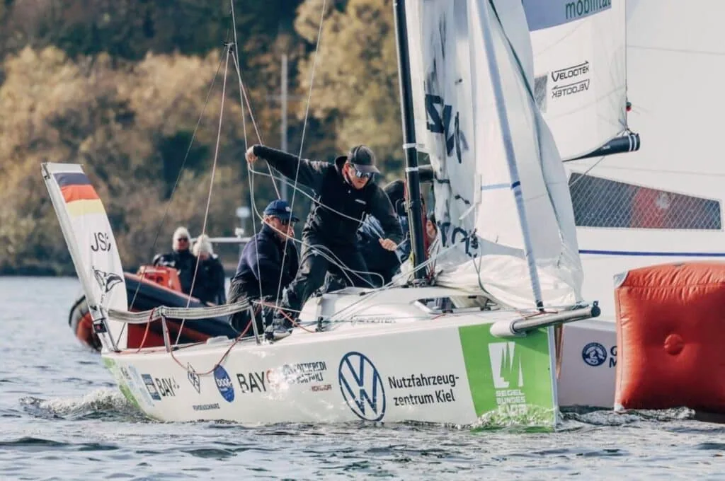 J/70 crew hiking hard as they round a mark at the Bundesliga Finals, VW and Bay sponsor logos on the hull
