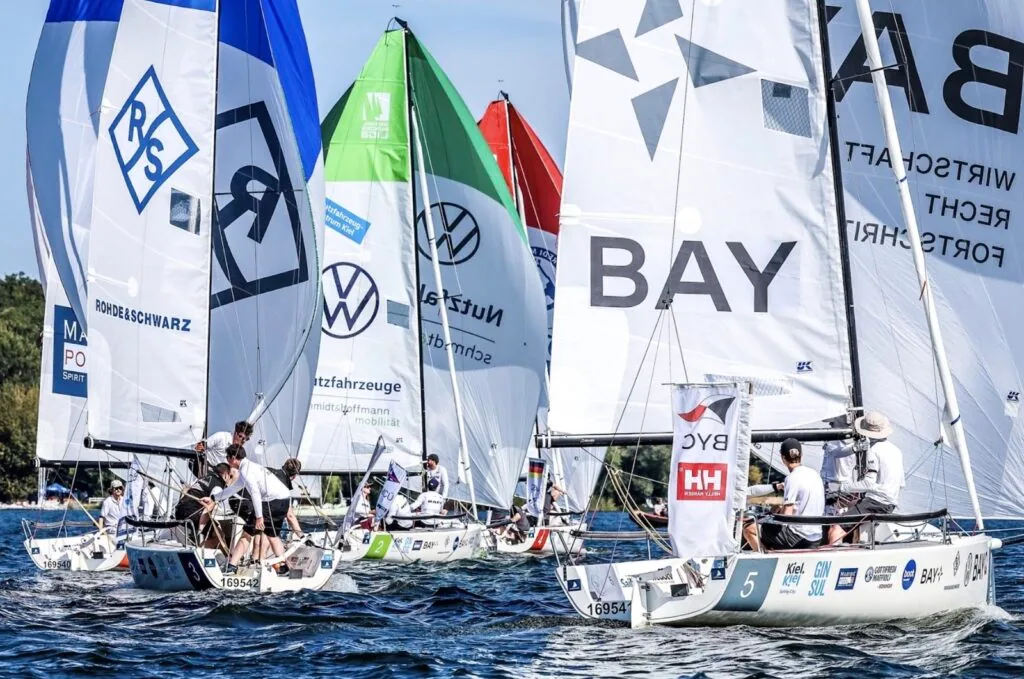 J/70 fleet reaching under colorful sponsor-branded spinnakers at the Bundesliga Finals